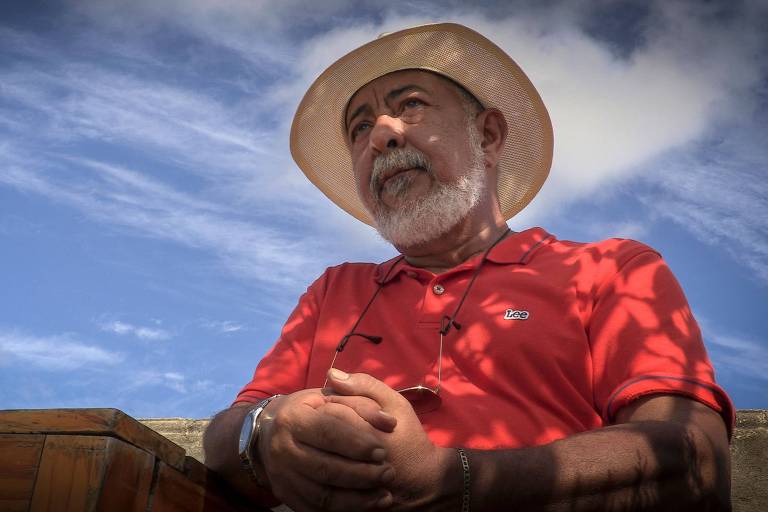 homem de barba branca, chapéu e camisa vermelha de mãos entrelaçadas