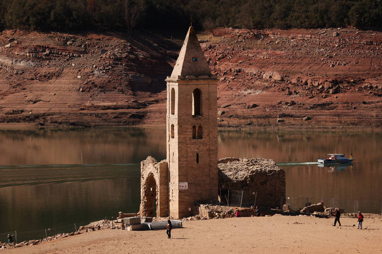 Turistas caminham perto de torre de igreja que emergiu em Sau, na Espanha, após queda do nível da água em um reservatório 