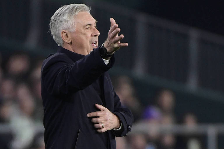 Imagem colorida mostra o técnico Carlo Ancelotti, um homem de 63 anos, da cintura para cima, virado para o lado direito e gesticulando com a mão direita