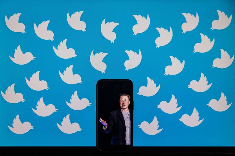 Elon Musk selou a compra do Twitter por US$ 42 bilhões em 28 de outubro de 2022. Ilustração mostra celular com foto de Musk, cercado por logos da rede social --a silhueta de um pássaro banco em fundo azul bebê.