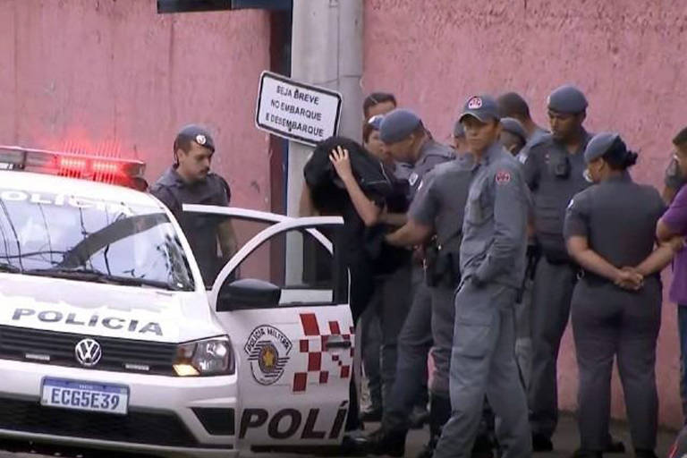 Policiais conduzem adolescente, com rosto coberto, a viatura