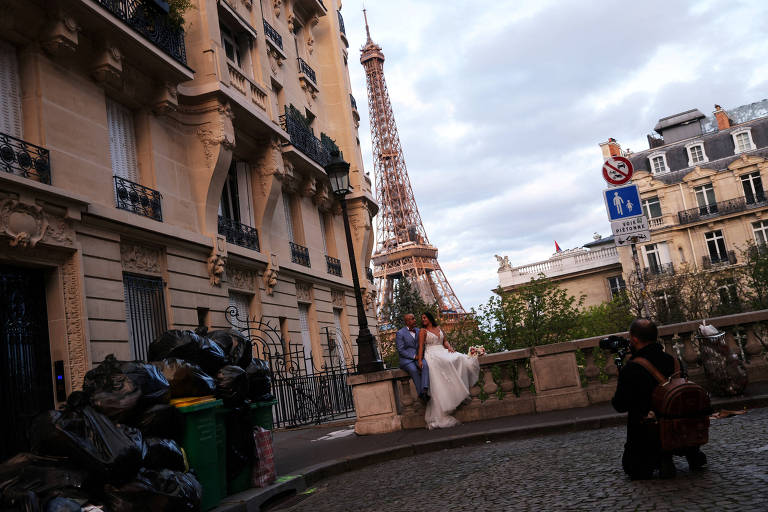 Casal posa para fotos tendo a Torre Eiffel aos fundos e próximos de lixo empilhado nas ruas durante protestos em Paris