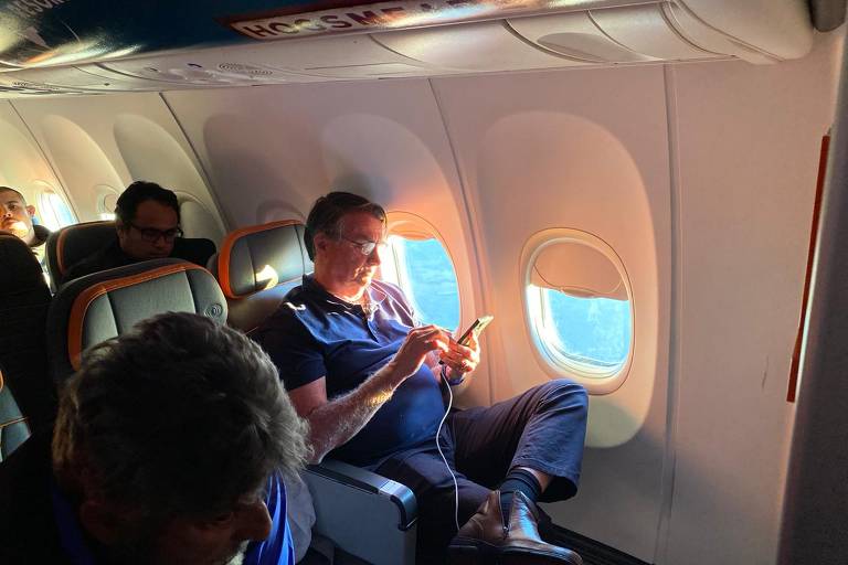 O ex-presidente Jair Bolsonaro (PL) usa o celular no avião que o trouxe de volta ao Brasil
