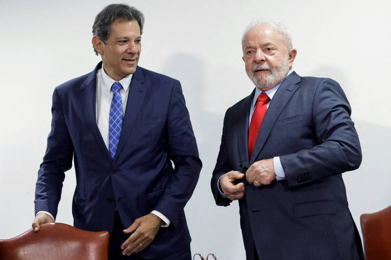 Lula e Haddad vestem ternos azul-marinho e camisas brancas. Haddad usa gravata azul, e Lula, vermelha.