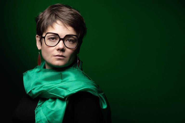 Retrato de Lucie, que usa óculos de armação preta e echarpe verde