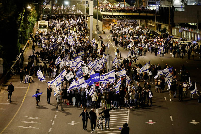 a foto, tirada à noite, mostra milhares de manifestantes andando numa rodovia com bandeiras de israel, nas cores azul e branca