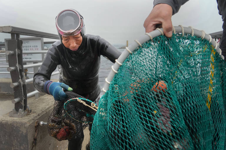 Idosa usando máscara e roupa de mergulho segura redes com algas marinhas e frutos do mar