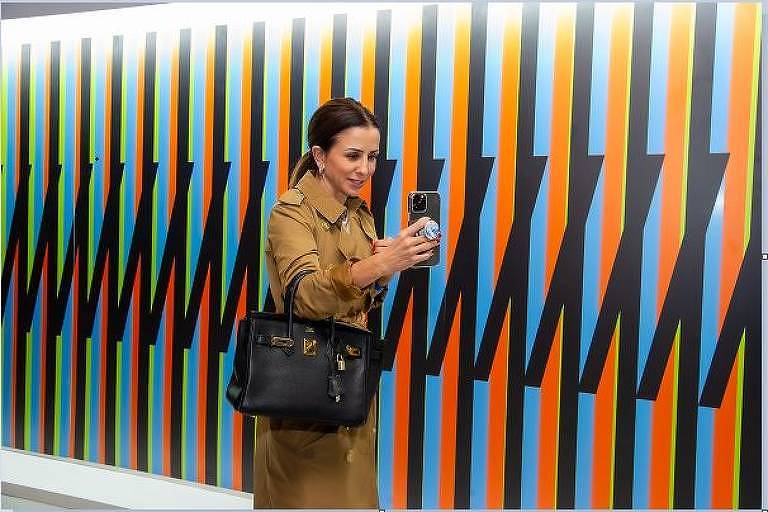 Uma mulher de vestido marrom usa seu celular para fotografar um painel colorido
