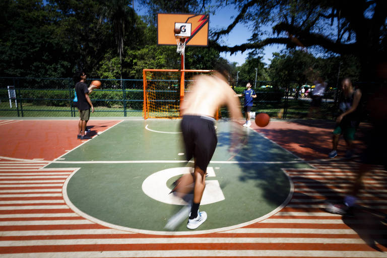 Rapazes jogam basquete em quadra no parque