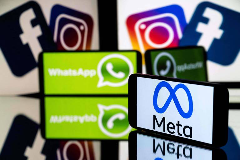 Foto mostra dois smartphones: um com logo da Meta e outro com logo do WhatsApp. Ao fundo estão duas telas de computador com a mesma imagem: logos de Facebook e Instagram.
