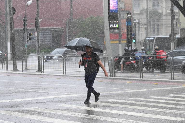 Pedestre atravessa rua segurando guarda-chuva