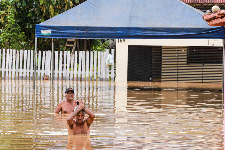 Imagem colorida mostra dois homens andando na enchente na cidade de Rio Branco, no Acre. A água chega na altura do peitoral dos dois homens que aparecem sem camisa. 