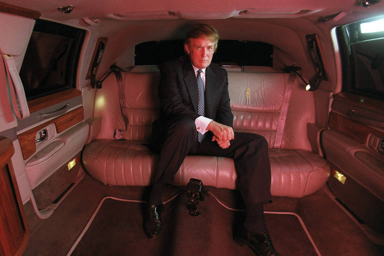 Homem loiro de terno sentado em banco traseiro de carro