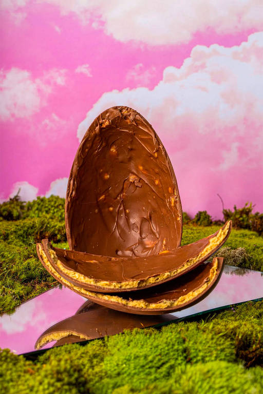 A foto mostra um ovo de chocolate aberto com uma das cascas partida ao meio. No recheio-o nota-se uma pasta de castanha com pedacinho de chips de batata