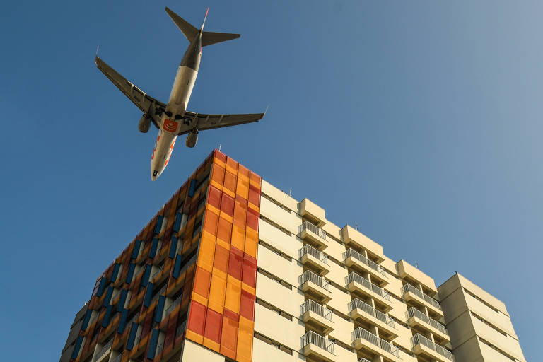 Imagem mostra avião sobrevoando perto de prédio.