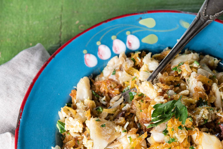 Sob fundo verde, um prato azul guarda receita de bacalhau à Gomes de Sá da chef Heloisa Bacellar