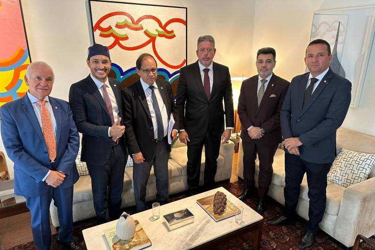 Deputados em pé (um deles com bandana na cabeça) posam para foto em uma sala, com um quadro ao fundo