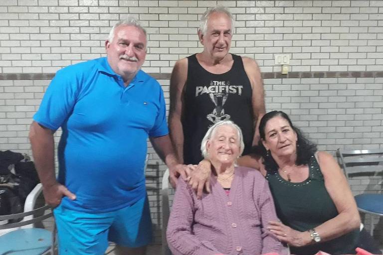 Adelina Bercelie Massucato, que morreu no último dia 27 de março, aos 98 anos, sentada em uma mesa com os filhos Armando, Nivaldo e Lourdes