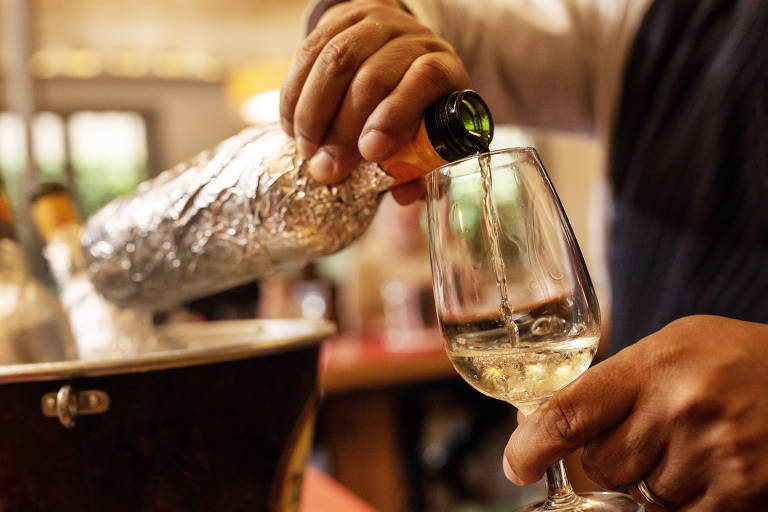 Rótulo de vinho encoberto com papel-alumínio é segurado e seu líquido colocado em uma taça