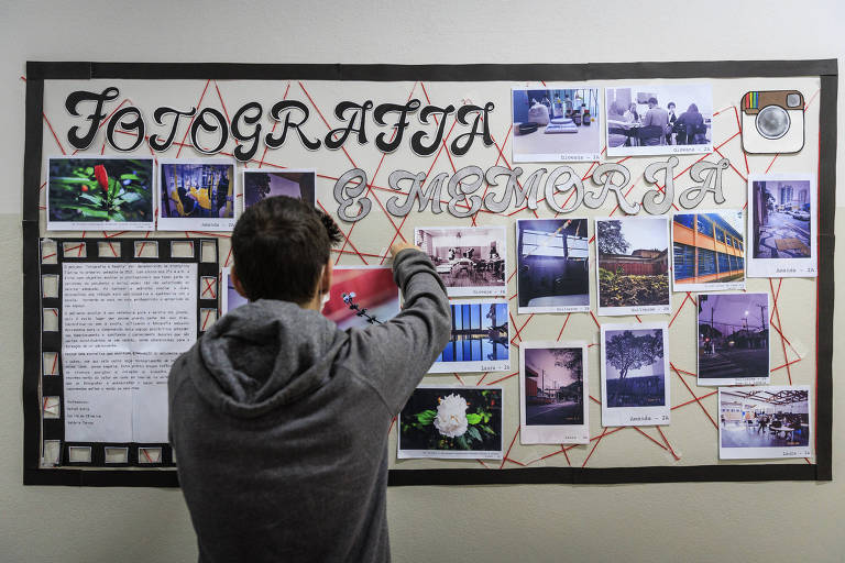 Estudante ajeita mural de fotografias em parede da escola