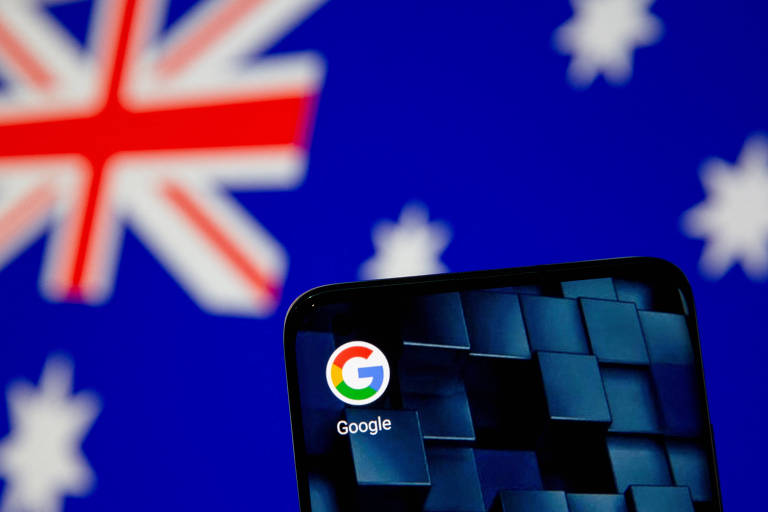 Imagem mostra smartphone com ícone do Google, em frente a uma bandeira da Austrália - lei australiana de remuneração de conteúdo jornalístico pelas Big Tech inspira legislação em vários países. 

