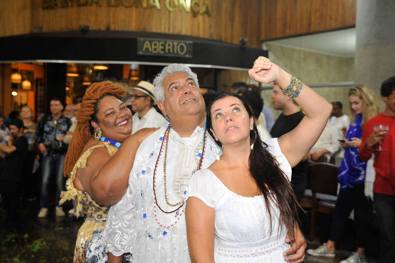 A foto mostras os chefs Dona Carmem Virgínia, Carlos Ribeiro e Janaína Torres Rueda vestidos de branco e dourado em frente ao Bar da Dona Onça