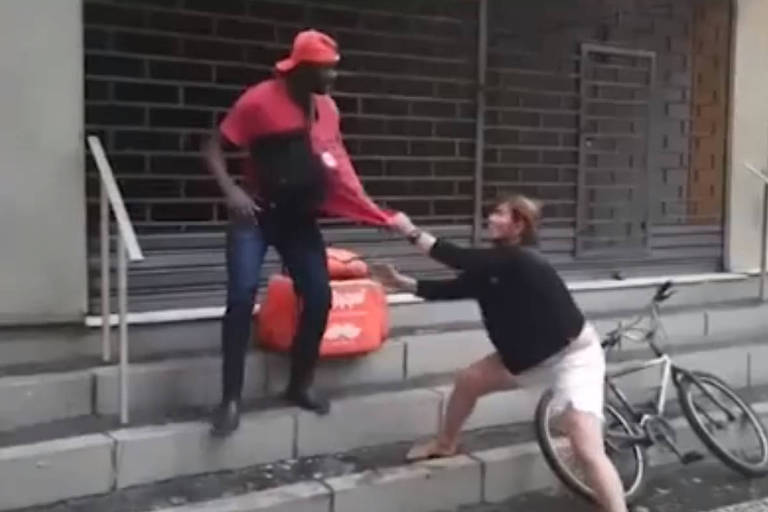 Na imagem, mulher branca segura camisa de homem negro para agredi-lo
