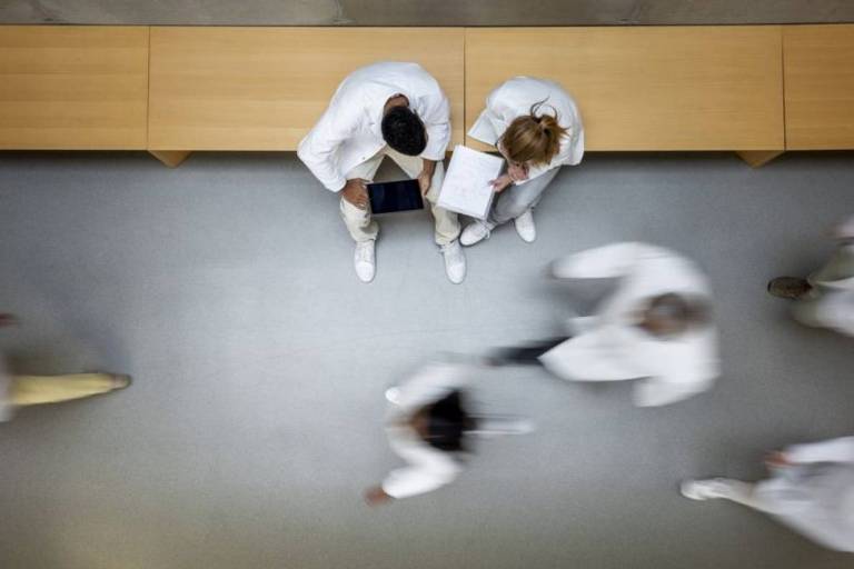 Corredor de um hospital visto de cima para baixo, mostrando pessoas de jaleco branco passando