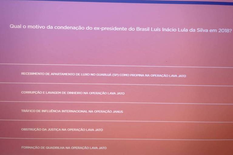 Tela vermelha com texto em letras brancas mostra pergunta com cinco alternativas e reproduz Reprodução de tela de teste, com pergunta sobre a prisão do presidente Lula 