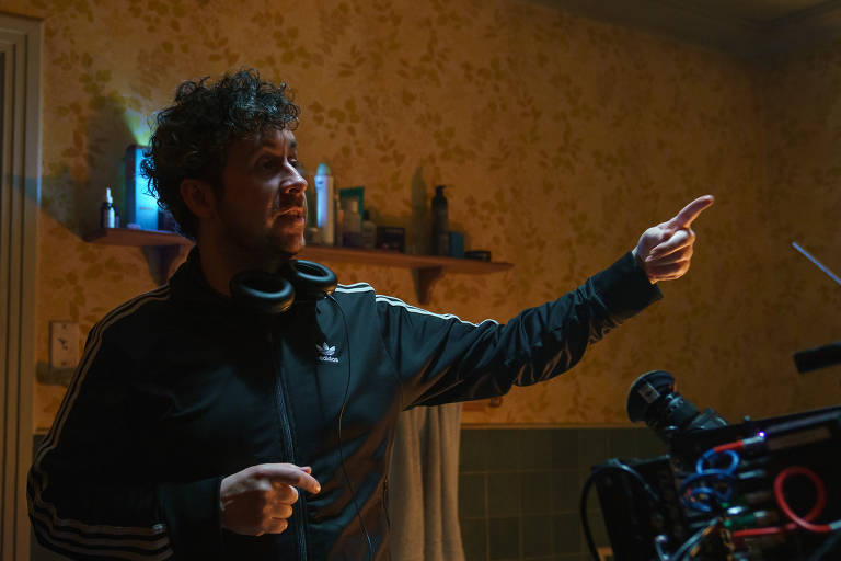 O diretor Lee Cronin, usando uma jaqueta escura, no set do filme 'A Morte do Demônio', apontando com o dedo indicador esquerdo para o canto direito da imagem