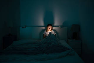 Sleepy woman lying in bed using smartphone late at night, can not sleep. Insomnia, addiction concept