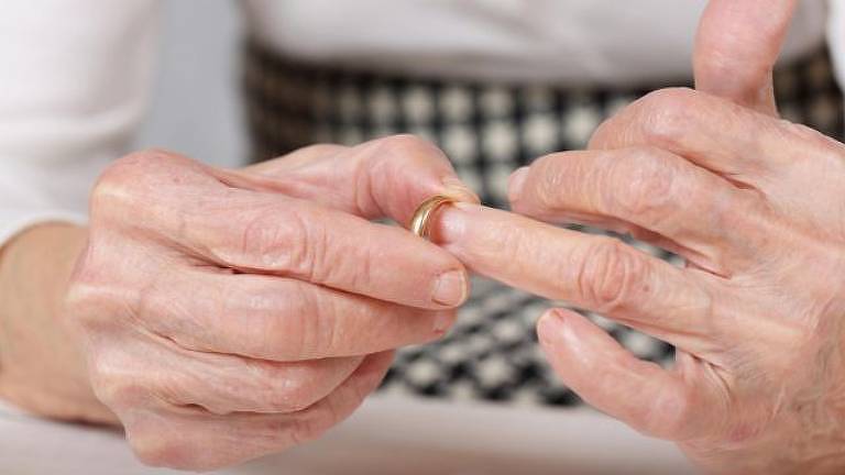 Mãos de uma pessoa idosa removem uma aliança dourada de casamento do dedo anelar da mão esquerda
