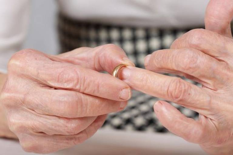 Mãos de uma pessoa idosa removem uma aliança dourada de casamento do dedo anelar da mão esquerda