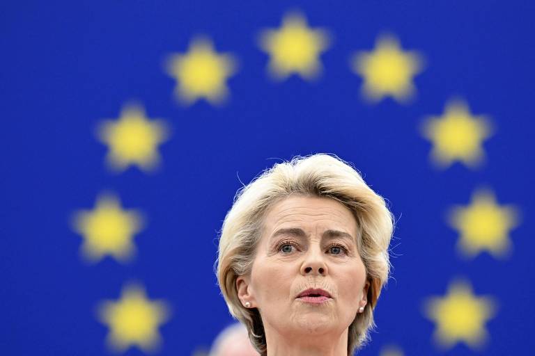 Foto mostra a cabeça da presidente da Comissão Europeia, Ursula von der Leyen, mulher branca com cabelos lisos, curtos e claros, no centro de um círculo formado por estrelas com fundo azul que compõem a bandeira da União Europeia
