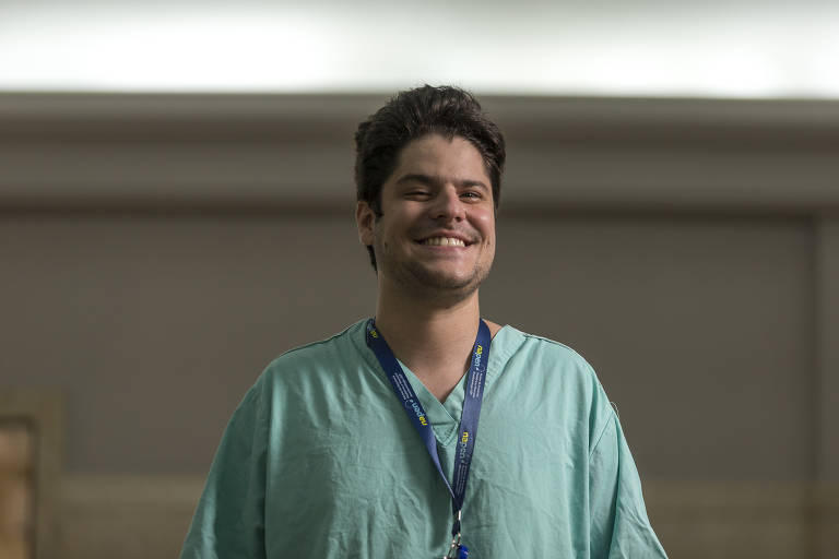 Imagem colorida mostra do tórax para cima Fernando Brito, um homem branco de 26 anos; ele veste um uniforme médico na cor verde