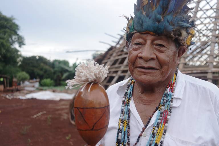 O indígena Atanásio Teixeira com cocar e um chocalho na mão