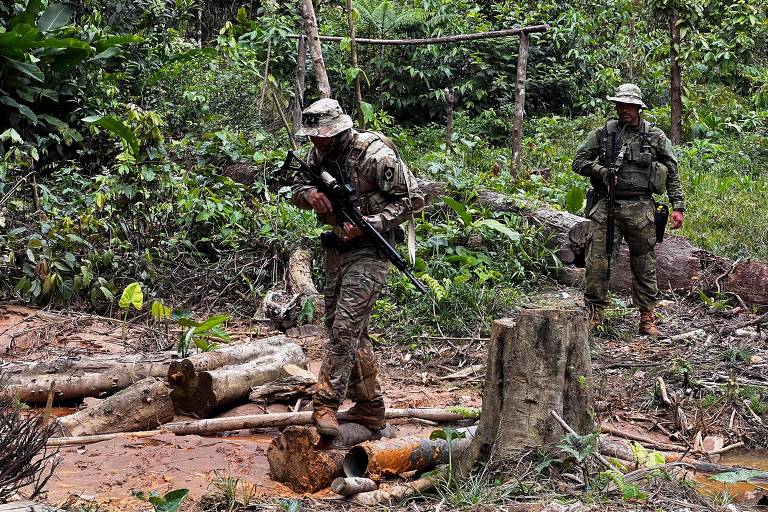Usando roupas camufladas e carregando armas, fiscais do Ibama circulam entre árvores cortadas durante operação de combate ao desmatamento e ao garimpo ilegal, na Terra Indígena Yanomami, em Roraima
