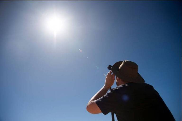 Homem observa o início do eclipse total do sol, protegendo os olhos com uma lente escura