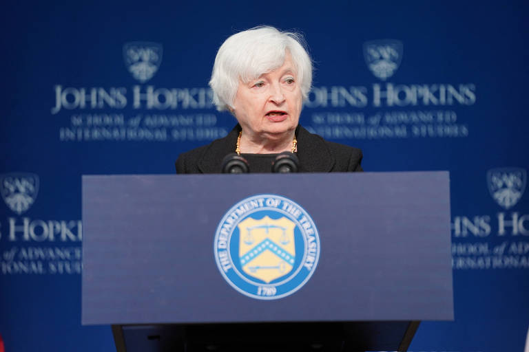 Foto mostra a secretária do Tesouro, Janet Yellen, mulher branca com cabelos brancos, em palanque azul em frente a um painel da mesma cor com "Universidade Johns Hopkins" escrito, em inglês, com letras brancas em vários locais