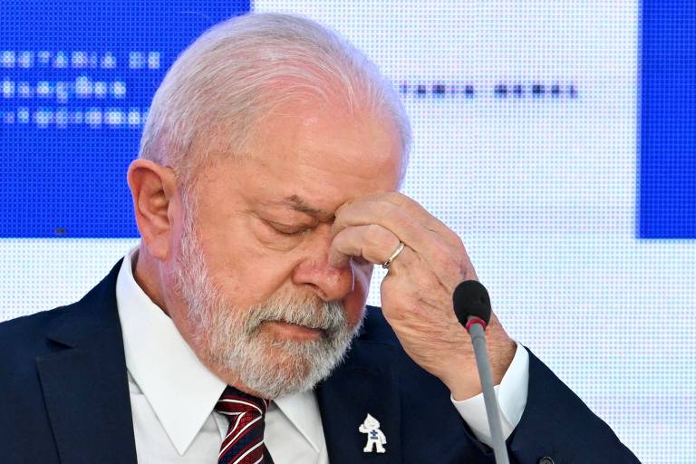 Com os olhos fechados e a mão no rosto, próxima ao olho esquerdo, o presidente Lula está de terno escuro e gravata listrada, durante a celebração dos cem dias de governo