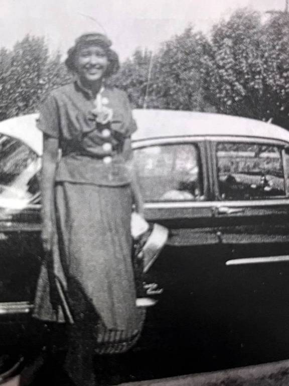 Uma mulher pousando para lateral de um carro antigo em uma foto e preto e branco