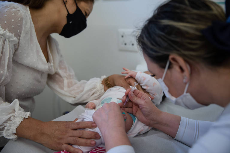 Enfermeira vacina perna esquerda de bebê, enquanto a mãe segurança a criança na maca