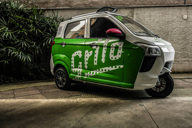 Imagem mostra veículo com uma roda dianteira e duas traseiras, com quatro portas, e carroceria pintada de verde e o logo da empresa: "Grilo"
