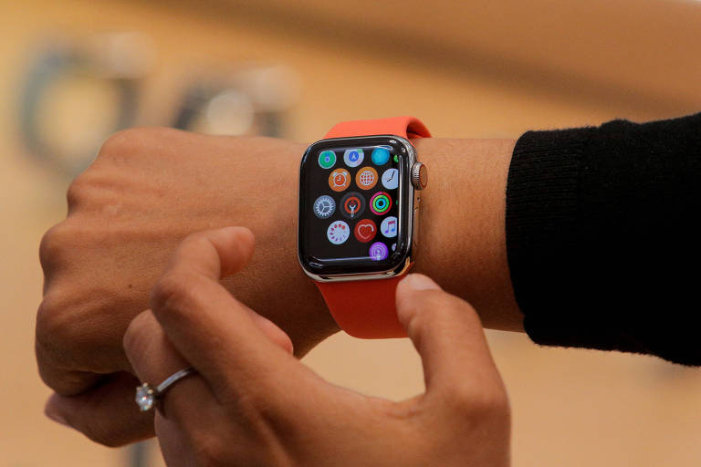Mulher veste Apple Watch Series 5, lançado em 2019. Relógio tem tela similar a de um smartphone, em dimensão compatível com um pulso. A pulseira é laranja e de borracha.
