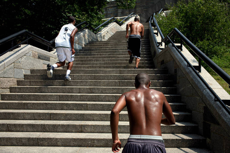 Homem negro de costas no canto da foto fazendo exercícios em uma escadaria ao ar livre