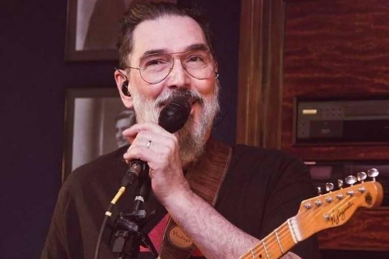 Em foto colorida, homem de barba branca canta enquanto toca guitarra em um estúdio