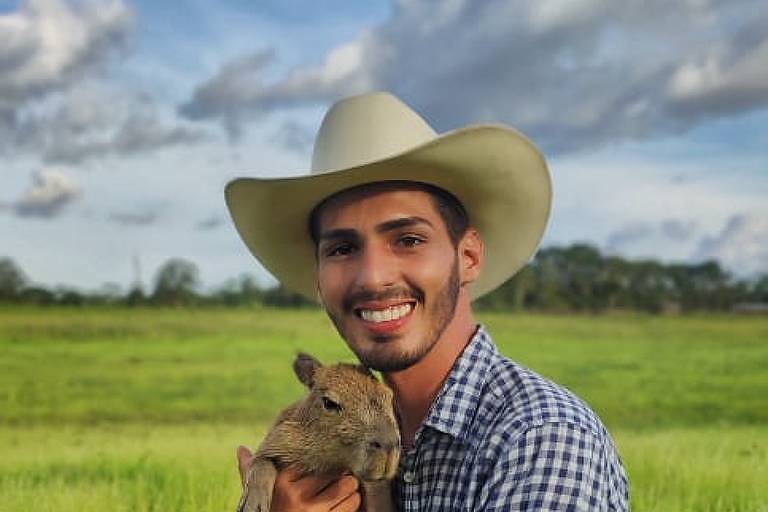 Jovem de camisa xadrez segura uma capivara bebê