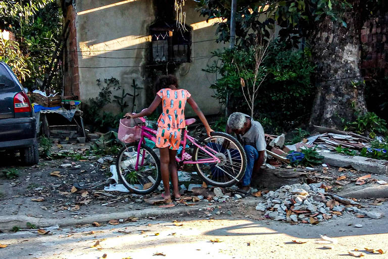 Homem conserta bicicleta para menina em Imbariê, Duque de Caxias, no Rio