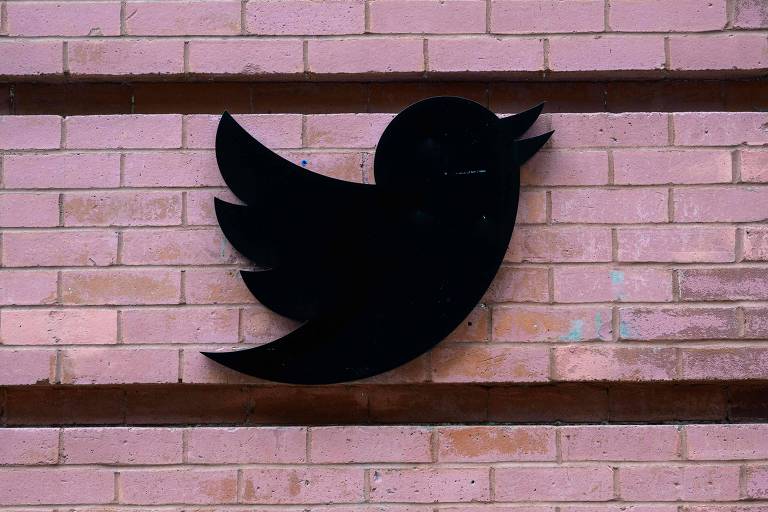 logotipo em preto do pássaro do Twitter, sobre uma parede de tijolos