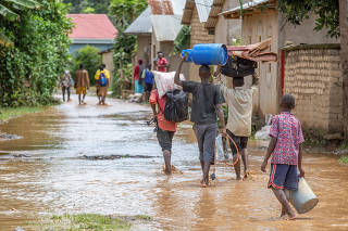 Residents wade through water after their homes were swamped following rains that triggered flooding and landslides in Rubavu district